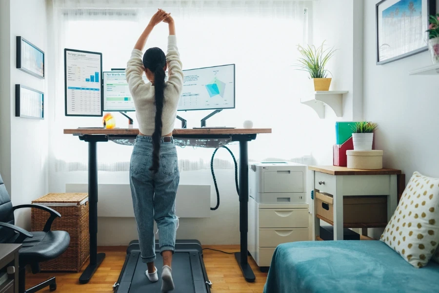 Woman working from home at standing desk is walking on under desk treadmill