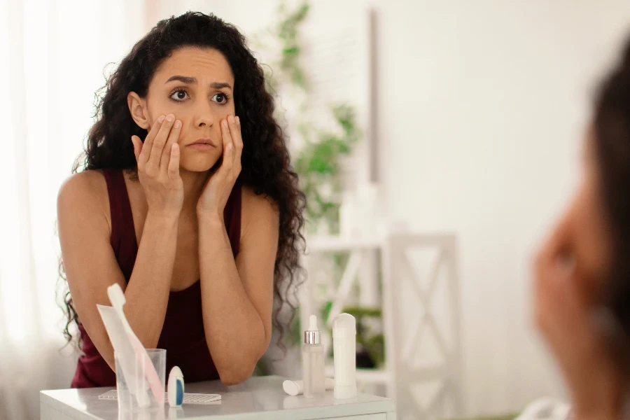 young woman looking in mirror and touching face
