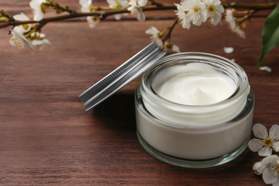 Jar of face cream and flowers on wooden table  