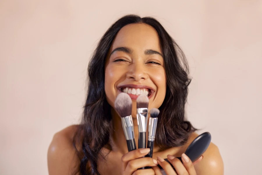 Cheerful latin woman holding cosmetic brushes to apply makeup
