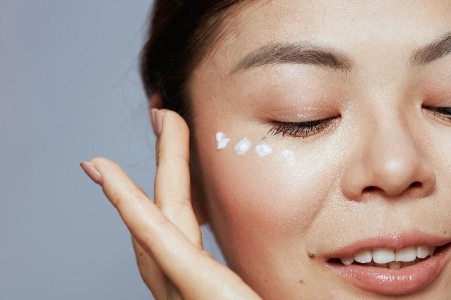 Closeup on modern asian female with facial cream on face isolated on blue background