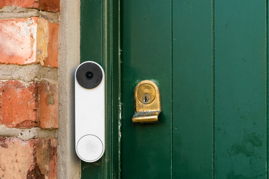 A video doorbell on a green door with a brass lock