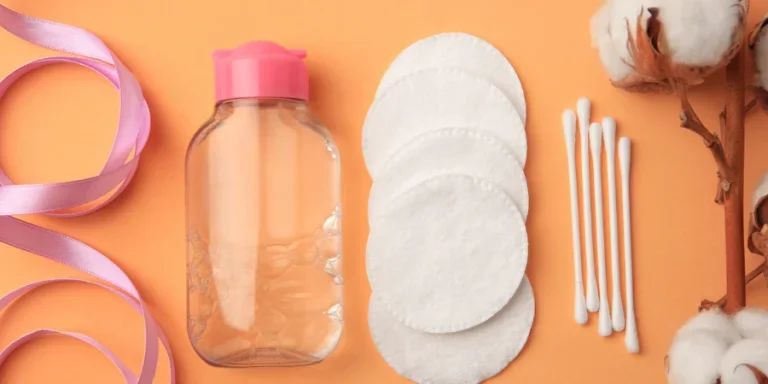 Flat lay composition with makeup remover and cotton flowers on pale orange background