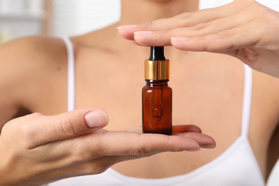 Woman with bottle of cosmetic serum on blurred background

