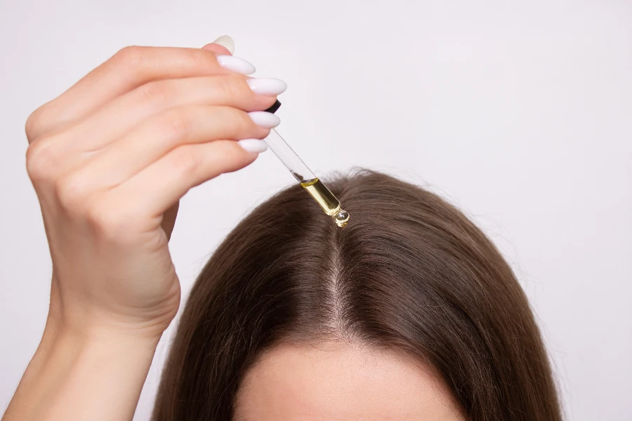 A young woman applies a drop of oil from a pipette to her scalp
