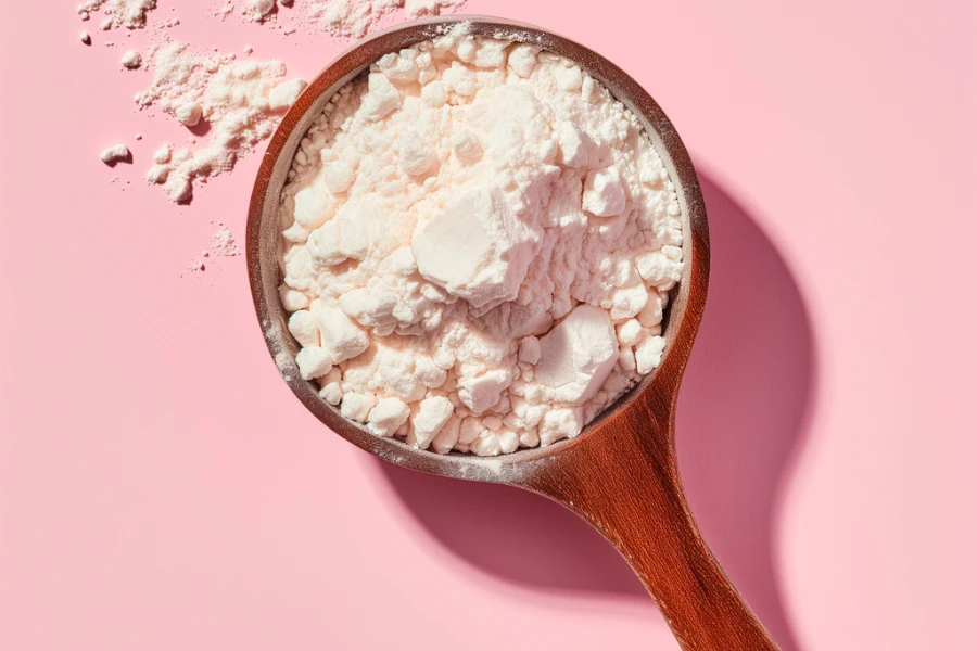 Measuring spoon with qasil powder or alginate mask on pink background
