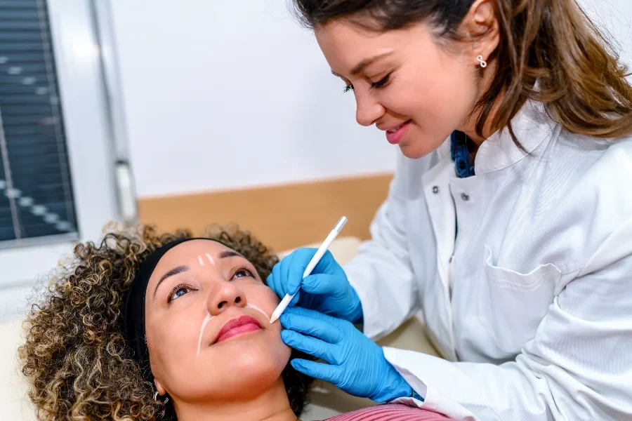 Beautician draw correction lines on woman face
