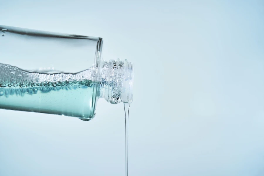 Cosmetic bottle from which serum is pouring on a blue background
