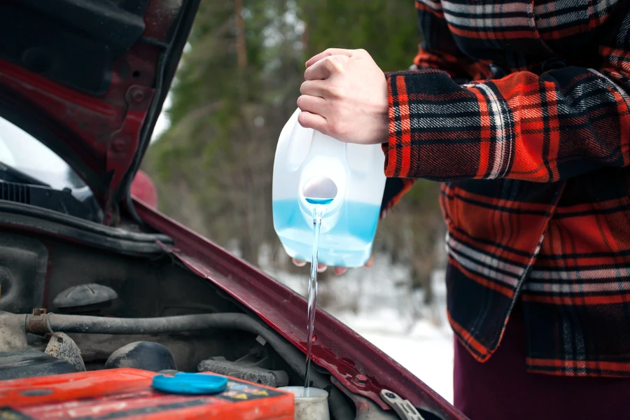 Young woman in a signal vest pours antifreeze into the car refrigerator on the highway