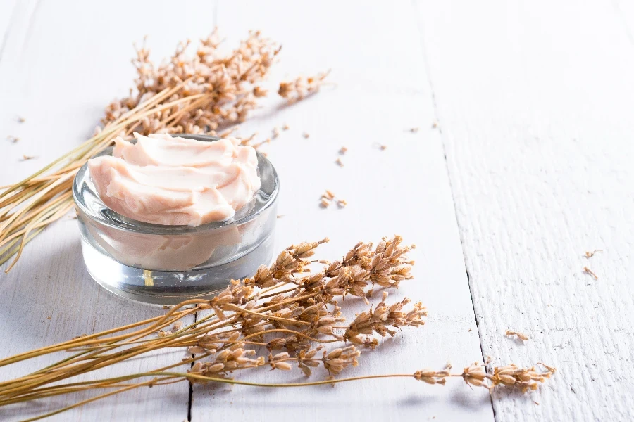 cosmetic cream and dried lavender flowers on white wooden table
