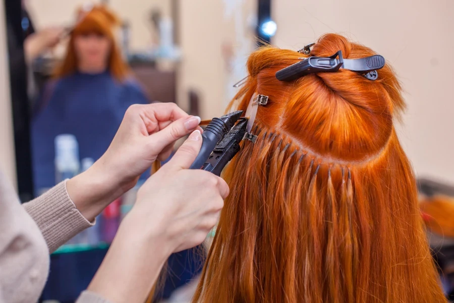 The hairdresser does hair extensions to a young