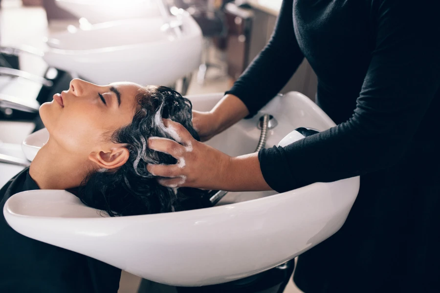 Woman applying shampoo and massaging hair of a customer
