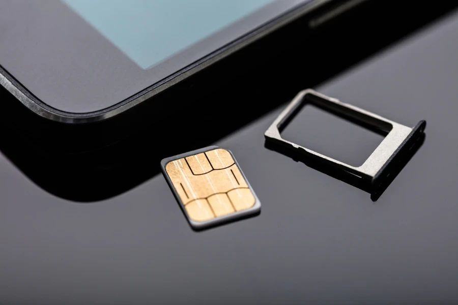 Close-up Of Sim Card Ready To Insert In Smart Phone Over The Desk