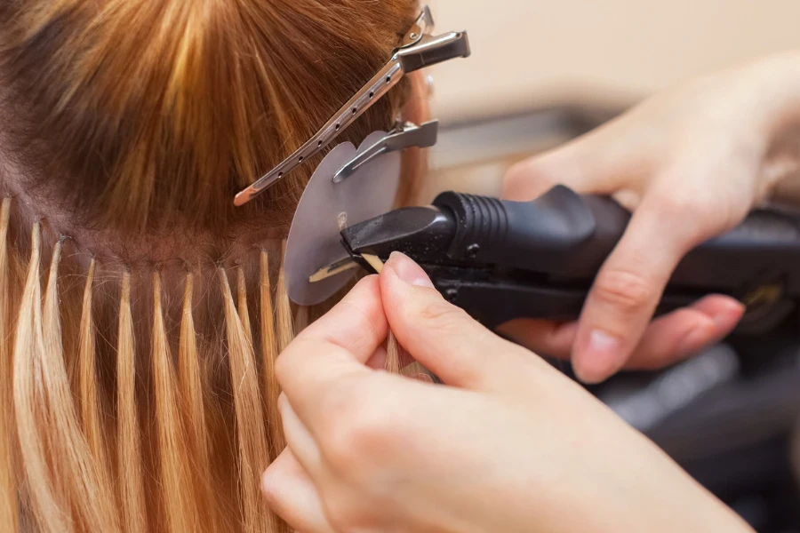 The hairdresser does hair extensions to a young girl
