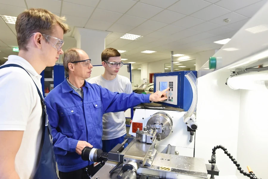 young apprentices in technical vocational training are taught by older trainers on a cnc lathes machine
