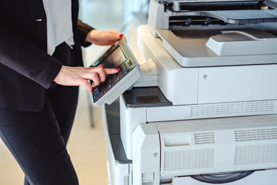 Woman standing and pressing button on a copy machine in the office
