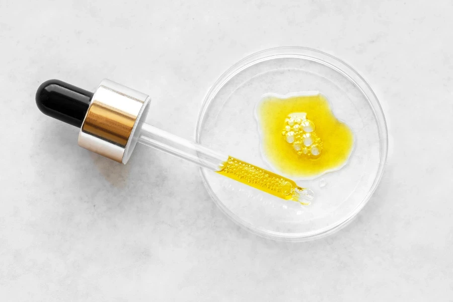 Liquid yellow retinol cosmetic serum or vitamin C gel or essential oil on petri dish close up