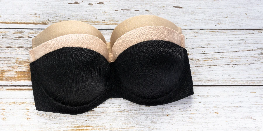 Set of black and beige strapless nude bra on a wooden texture background