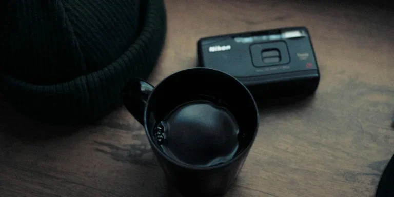 From above mug of hot beverage placed on timber table near retro point and shoot camera and hat