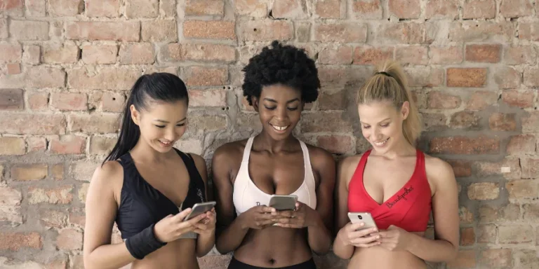Three Woman in Assorted-color Sport Bras Holding and Watching Their Smartphones