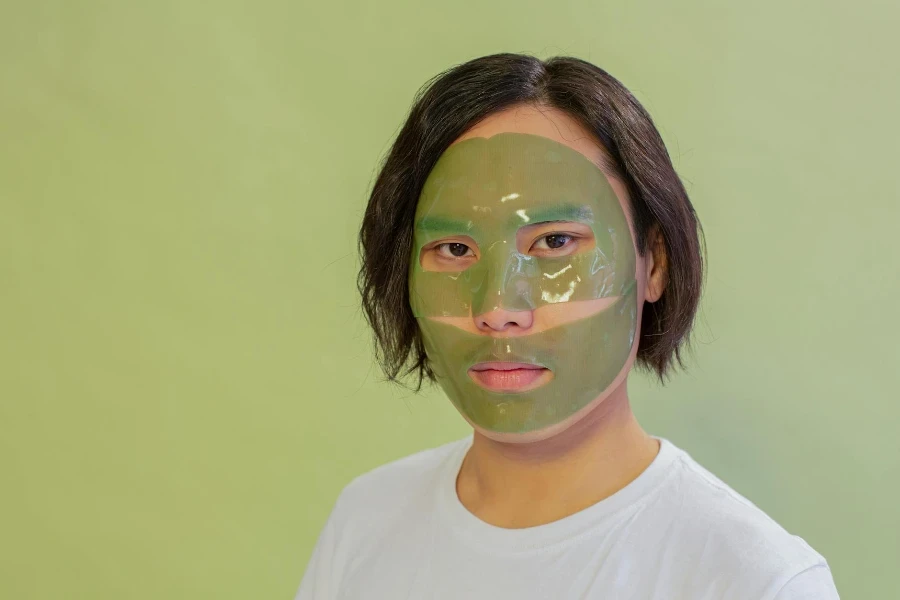 Calm Asian man with facial mask during cosmetic procedure 