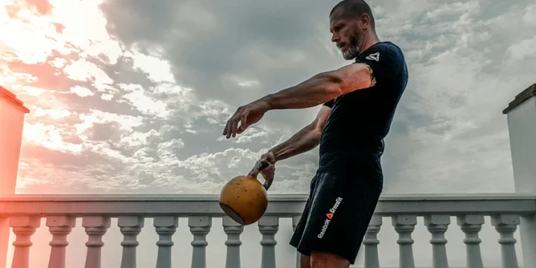 Man in Black Shirt Carrying Kettle Bell Outdoors