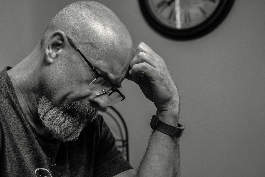 Grayscale Photo of Man Thinking in Front of Analog Wall Clock