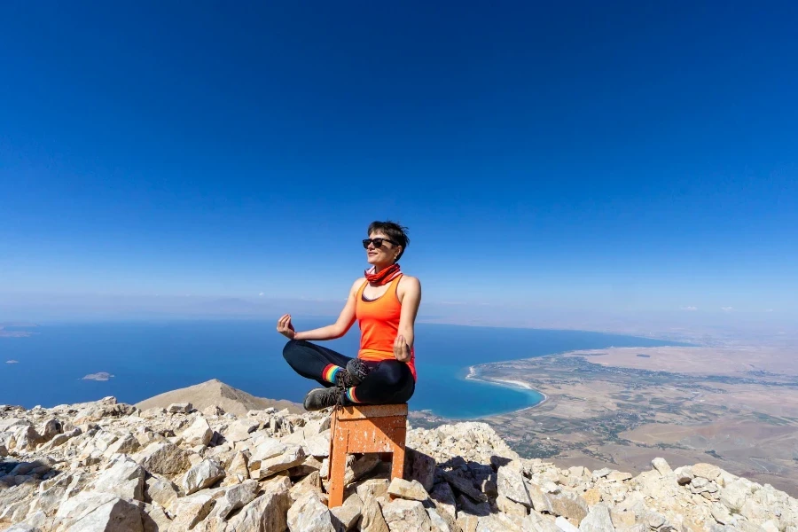 Woman in Orange Tank Top and Black Leggings Sitting on a Wooden Chair