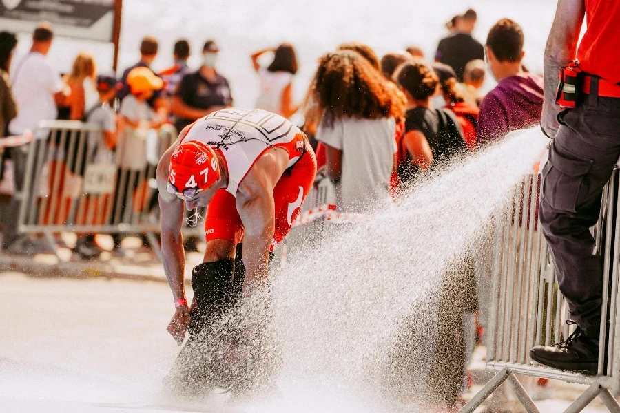 man washing fins of sportsman in active wear using hose with fast water flow during competition