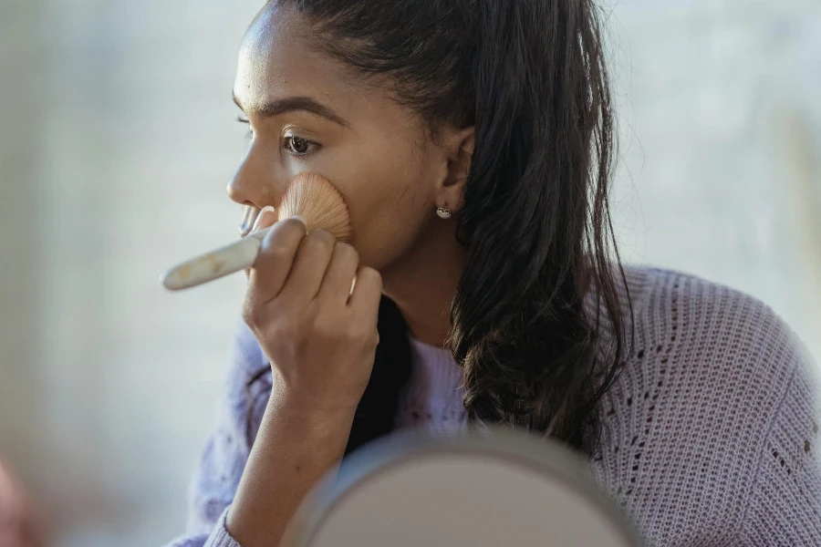 Black woman applying professional cosmetic on face with brush