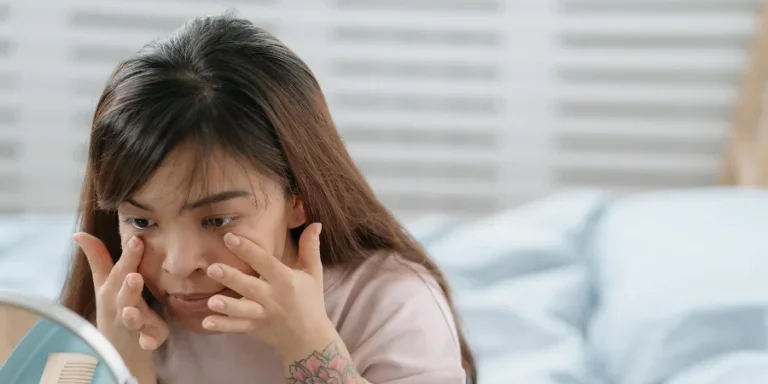 Young dwarf woman in bedroom rubbing face cream on skin under eyes