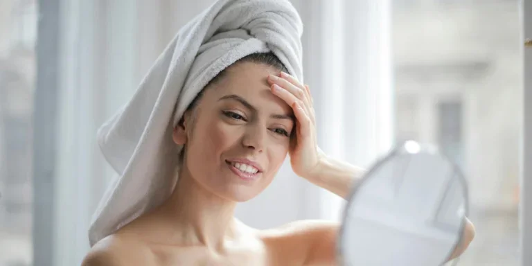 Selective Focus Portrait Photo of Smiling Woman With a Towel on Head Looking in the Mirror
