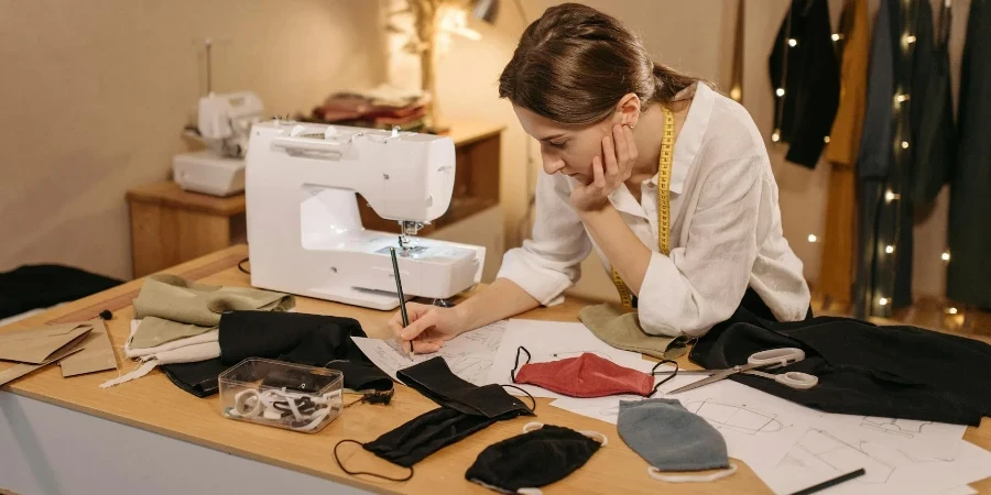 A Woman Drawing on a Paper while Making Face Mask Designs