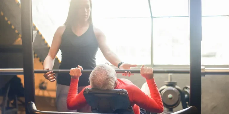 Woman in Black Tank Top Guiding an Elderly Man Doing Bench Press