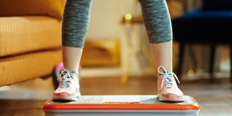 Closeup on young woman in fitness clothes in the modern house training using vibration power plate