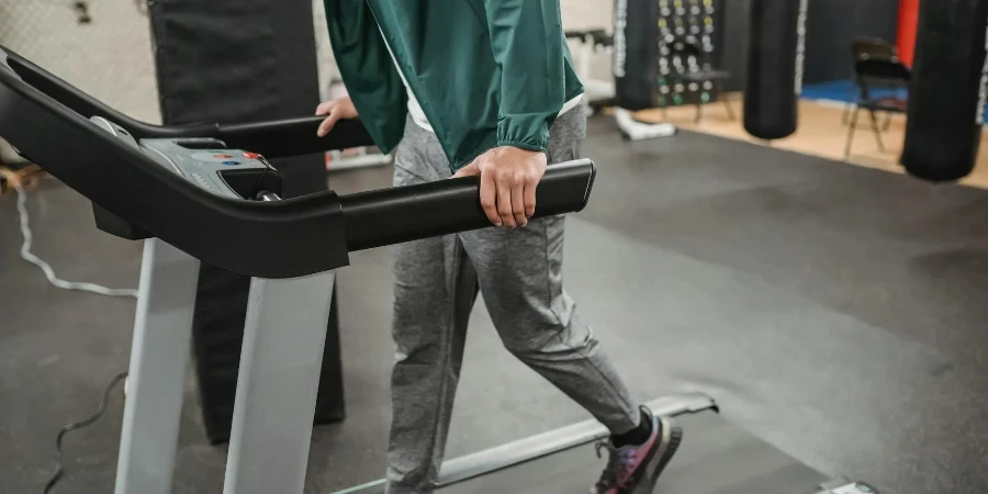 Crop anonymous male walking on contemporary treadmill in modern sport club with gym equipment