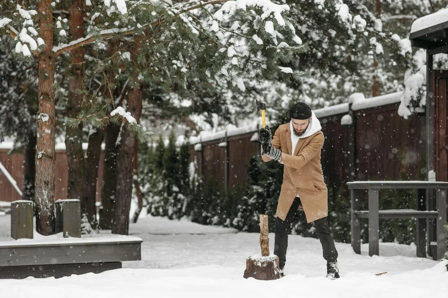 A Man in Brown Coat Standing on a Snow Covered Ground while Holding an Axe