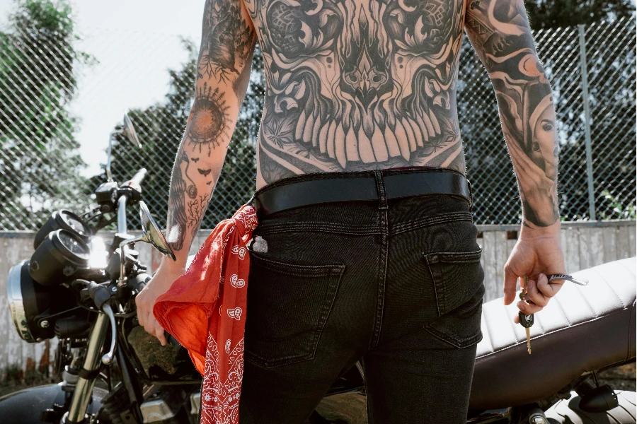 A Shirtless Tattoo Person Holding a Key in Front of a Motorbike