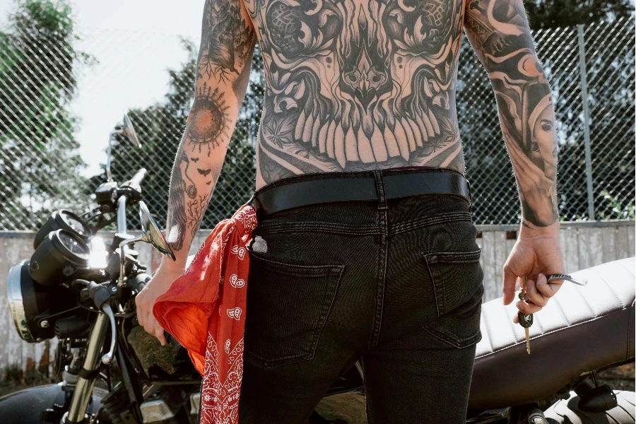 A Shirtless Tattoo Person Holding a Key in Front of a Motorbike