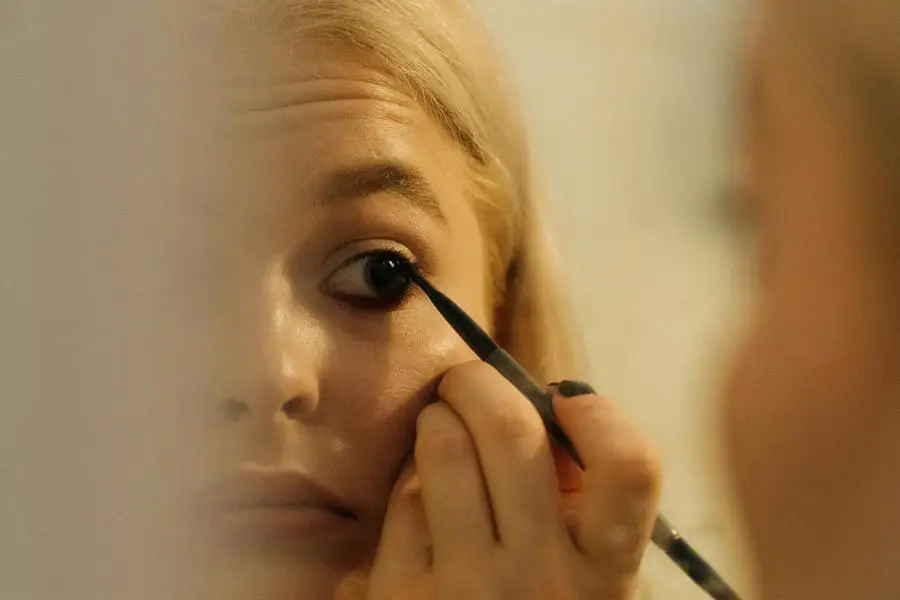 A Woman Looking at the Mirror while Applying Eyeliner by cottonbro studio