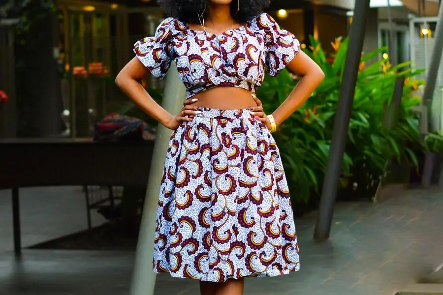 A Woman in White and Brown Matching Set Clothes Standing with Legs Crossed by Amani Nation