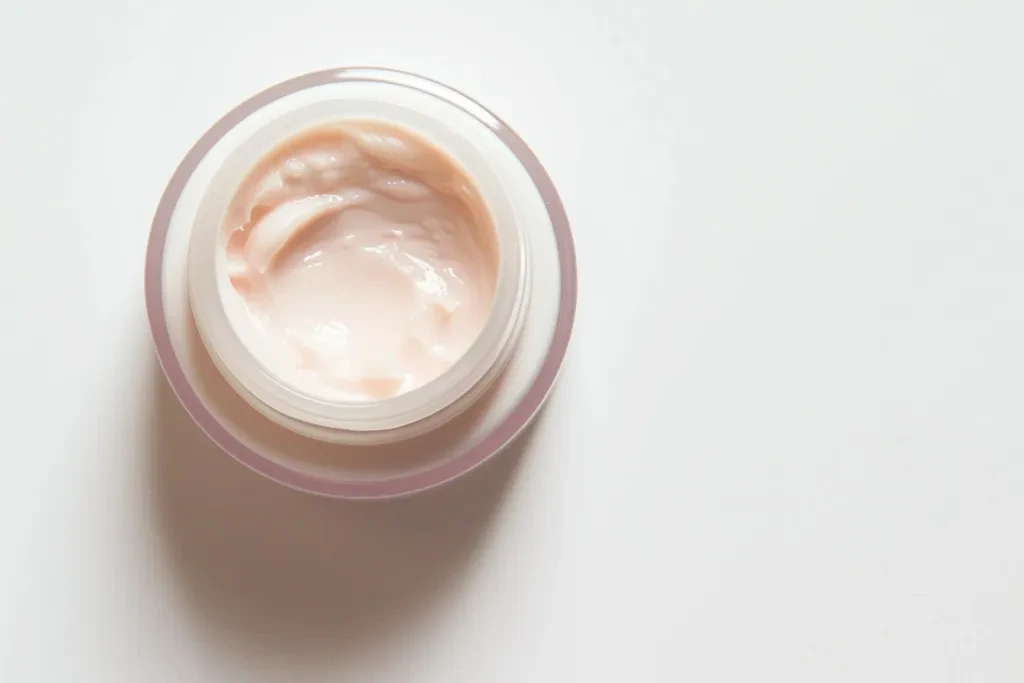 A close up shot of an open jar with light pink cream