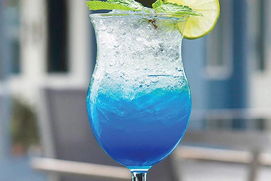 A hurricane glass with a blue cocktail and lemon