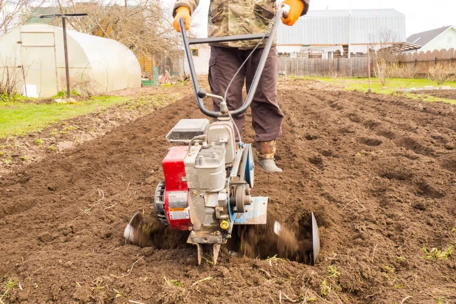 A man works the land in the garden with a cultivator, prepares the soil for sowing