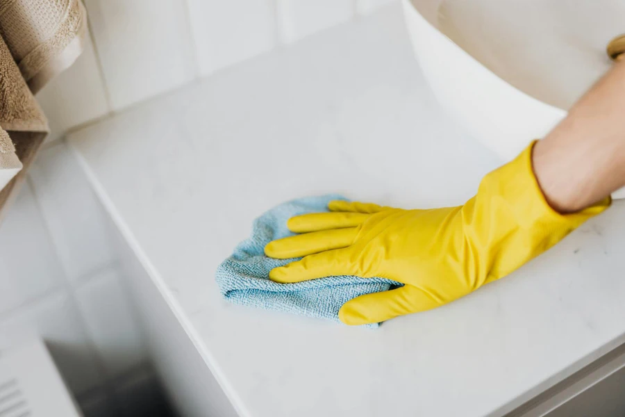 A person with microfiber cloth wearing yellow rubber glove and cleaning white marble