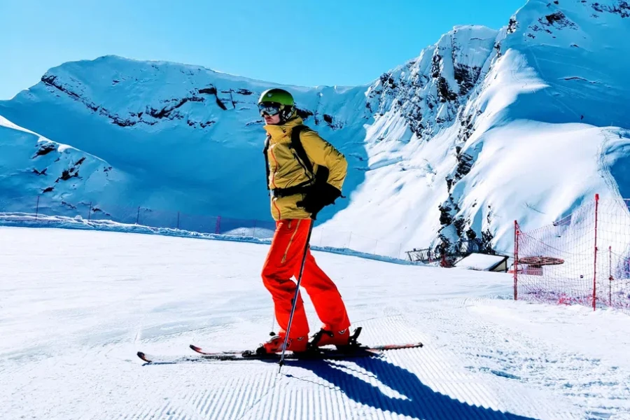 A skier in striking red pants surveys the snow-covered slopes, ready to glide down the freshly groomed trails under a clear blue sky. 
