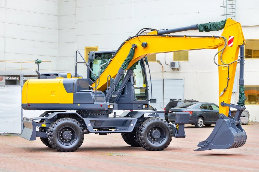 A wheeled construction excavator is parked in a paved car park on a bright day