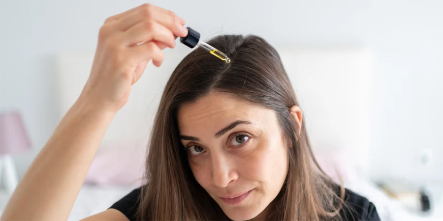 A woman applies essential oil drops to her scalp