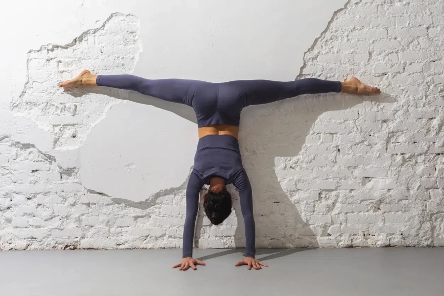 A woman trainer practicing yoga performs the Adho Mukha Vrikshasana exercise against the wall