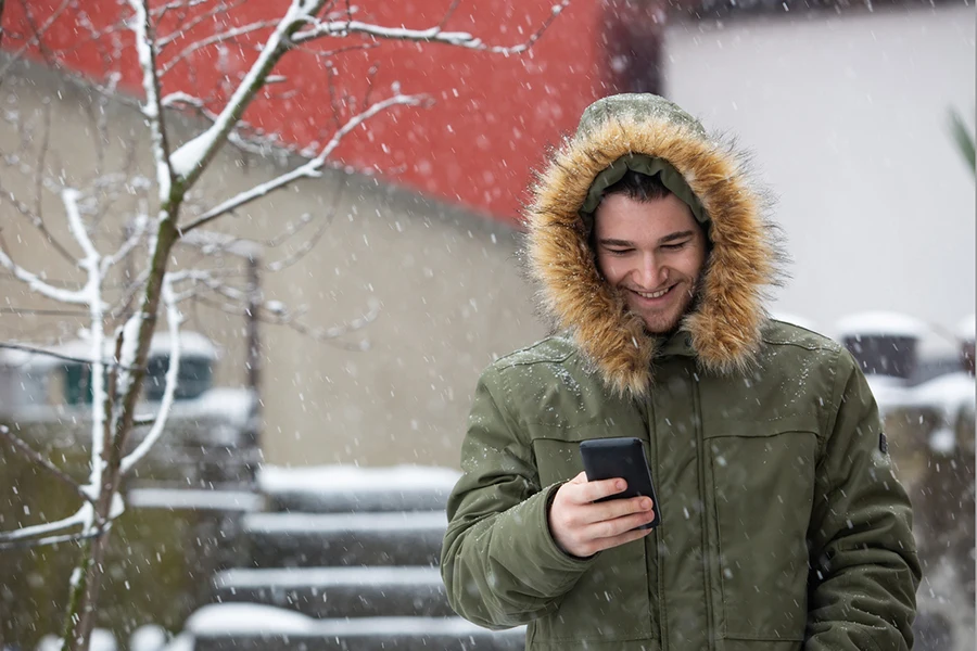 A young man exchanges text messages on a snowy day